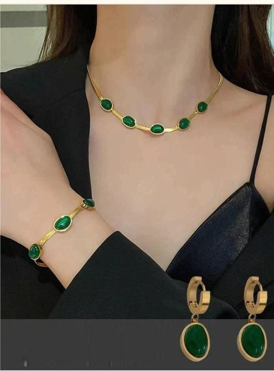 Gold jewelry set with green gemstones including necklace, bracelet, and earrings on a person wearing a black top.