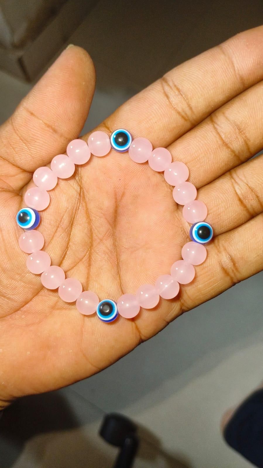 Hand holding a pink beaded bracelet with blue evil eye charms.