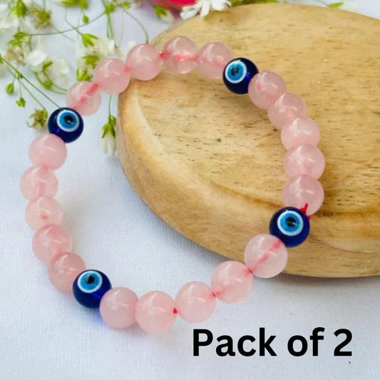 Pack of 2 pink beaded bracelets with blue evil eye charms on a wooden surface.