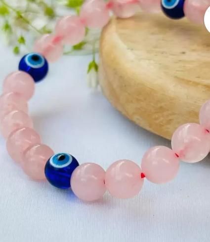 Pink beaded bracelet with blue evil eye beads on a white background